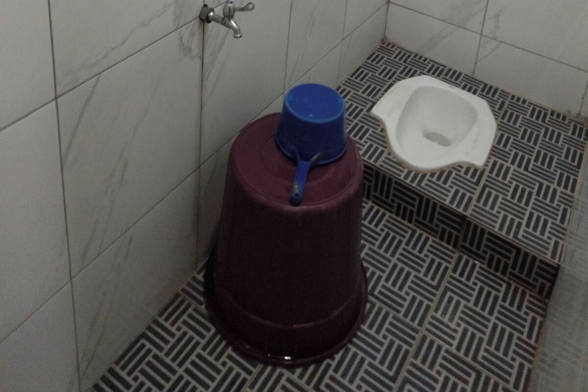 A small bathroom with a toilet, a blue water container, and a marble-patterned floor.
