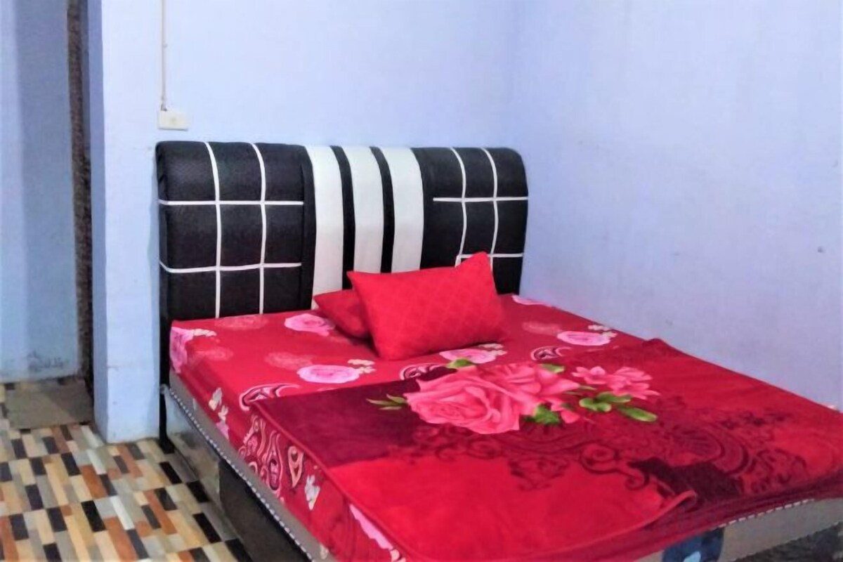 A bed with a black and white headboard, a red bedspread with floral patterns, and a single red pillow.