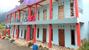 A two-story building with a balcony on the upper floor, featuring a patterned tile floor and a mix of red and blue structural elements. - Penginapan Puncak DP (Berastagi)