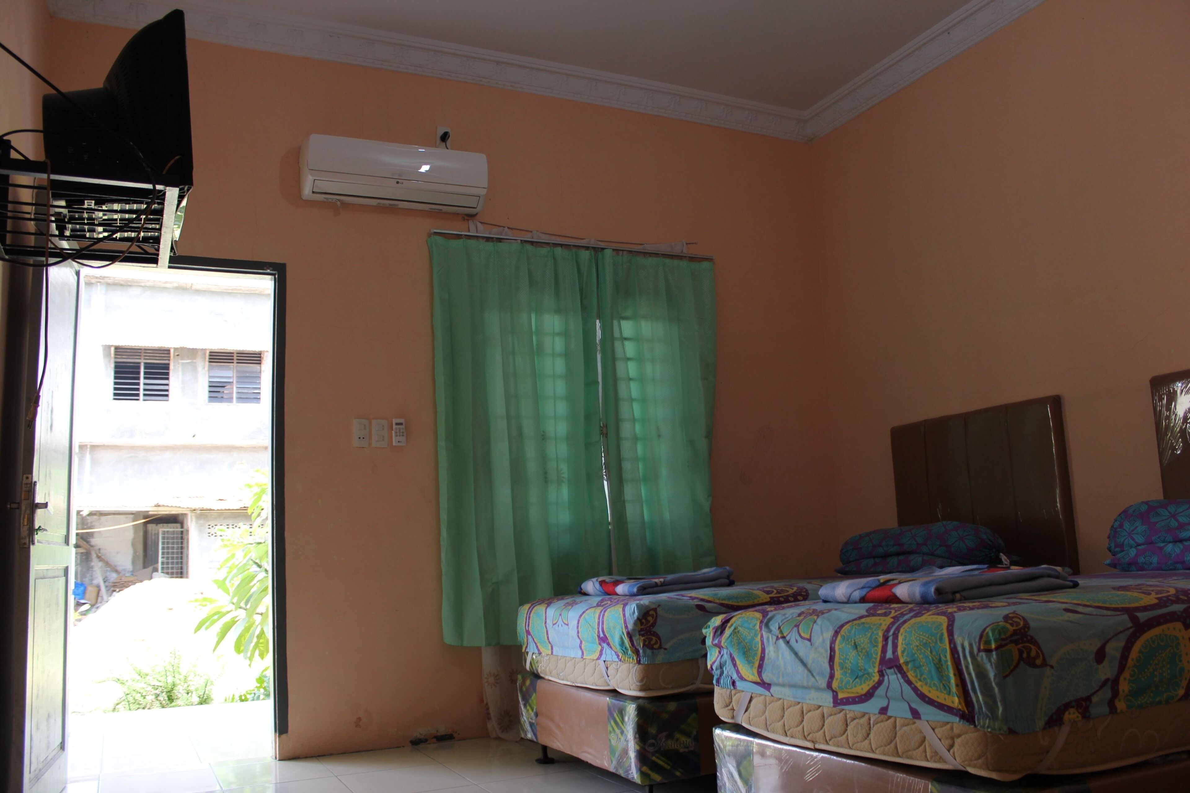 A room with two beds, an air conditioning unit, a green curtain, and a view of the outside.