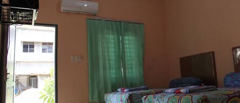 A room with two beds, an air conditioning unit, a green curtain, and a view of the outside.