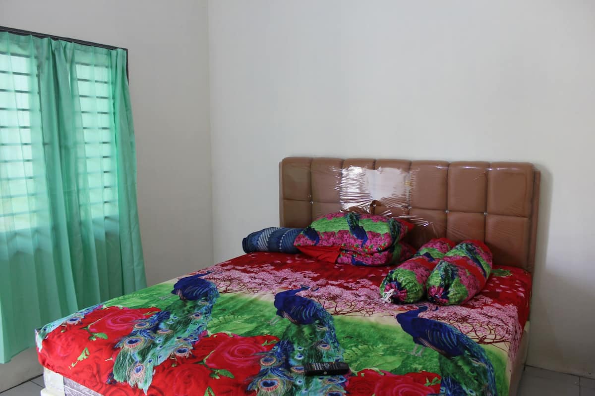 A bed with a floral and peacock-themed bedspread, a padded headboard, and a green curtain.