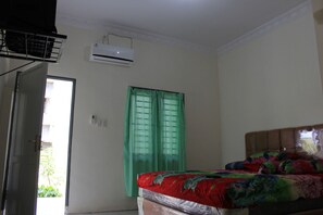 A room with a bed, an air conditioner, a door, and a window with green curtains. - Penginapan Transit Tomato (Medan)