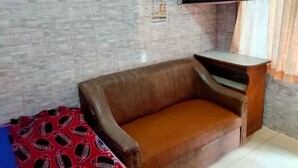 A room with a brown sofa, a small table, a television mounted on the wall, and a tiled wall with a blue border. - Hotel Rinosari Bandungan (Bandungan)