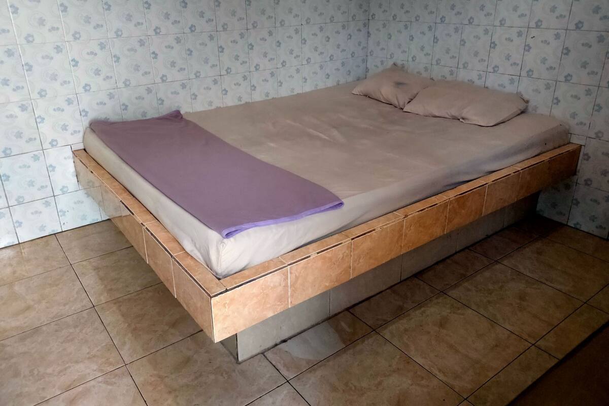 A single bed with a wooden frame and a mattress, a purple blanket, and two pillows.