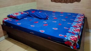 A bed with a blue floral bedspread and pillows, a brown headboard, and a brown curtain on a window. - Hotel Rinosari Bandungan (Bandungan)