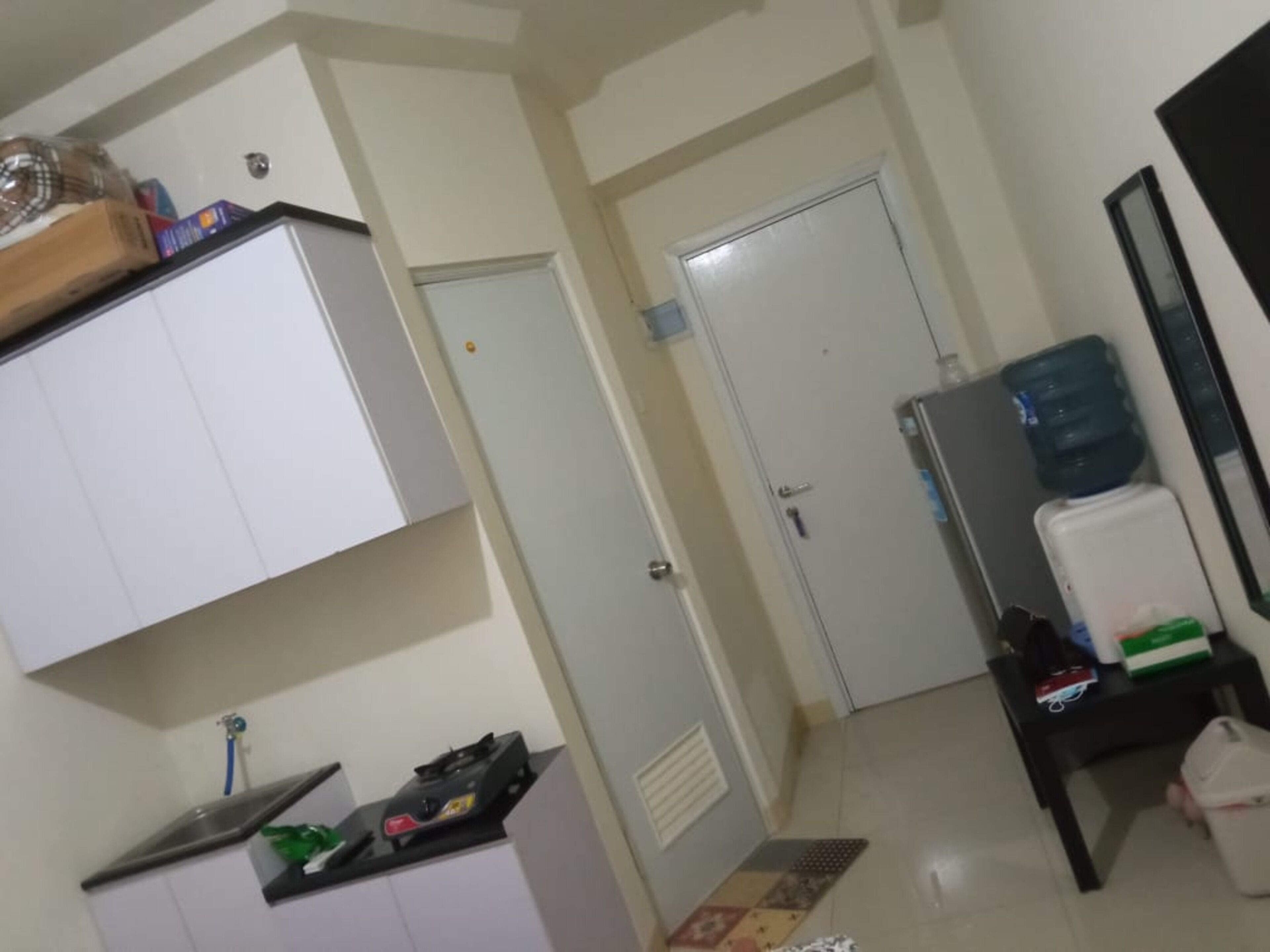 Une pièce avec une armoire blanche, une petite table avec un distributeur d’eau et une porte donnant sur une autre pièce.