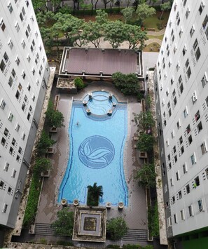 Une piscine sur le toit, entourée de gratte-ciel, avec un espace de détente circulaire et un terrain de volley-ball.