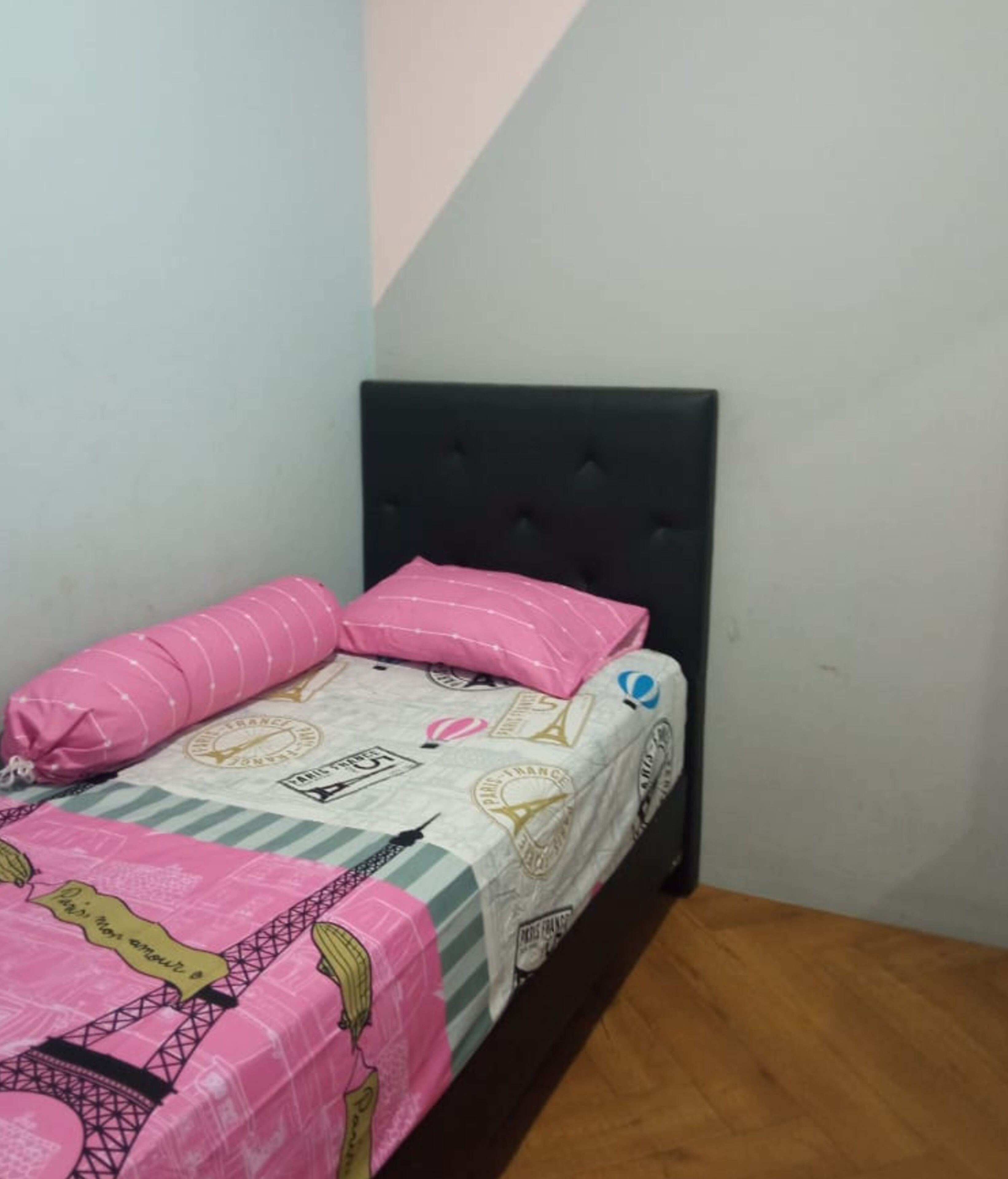 Een enkel bed met een zwart hoofdeinde, een roze en witte bedspreide en passende kussens.