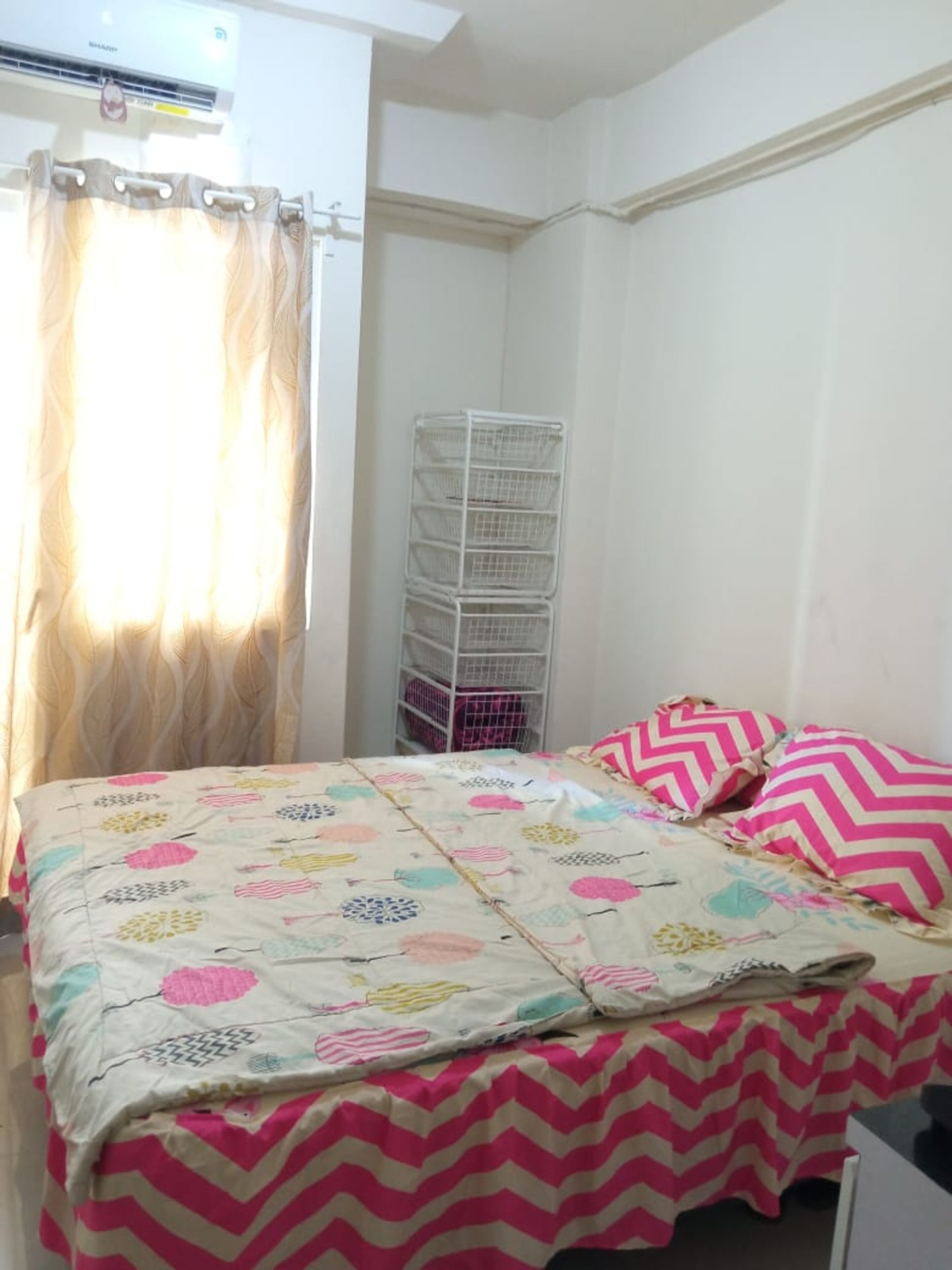 A bedroom with a bed, a white metal storage unit, and a window with curtains.