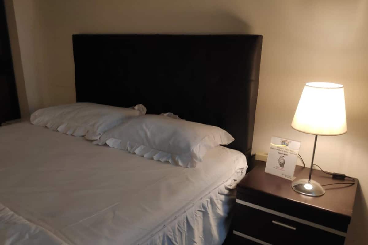 A neatly made bed with white linens, a dark headboard, and a bedside table with a lamp and a sign.