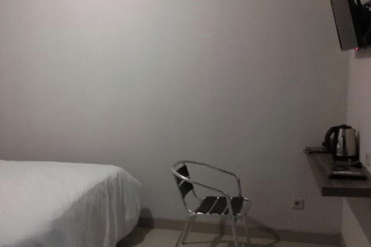 Une pièce comprenant un lit, une chaise et une petite étagère avec une bouilloire.