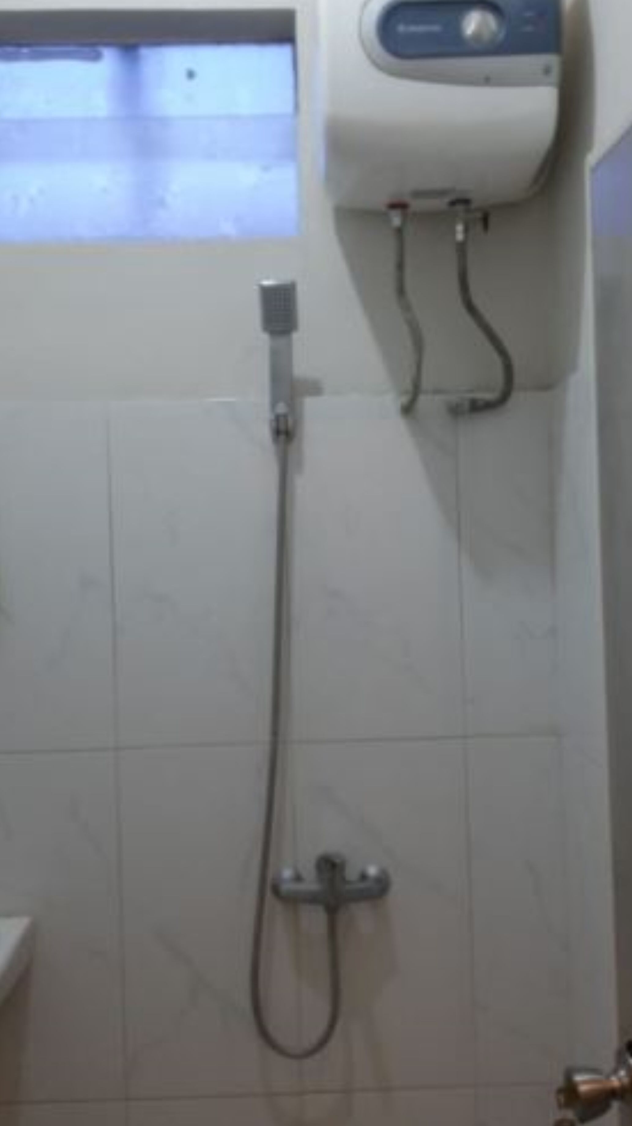 A bathroom with a shower, a hand dryer, and a towel dispenser.