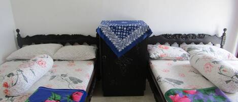 A room with two beds, each with floral bedding and a matching pillow. There is a small table with a blue cloth in the center.