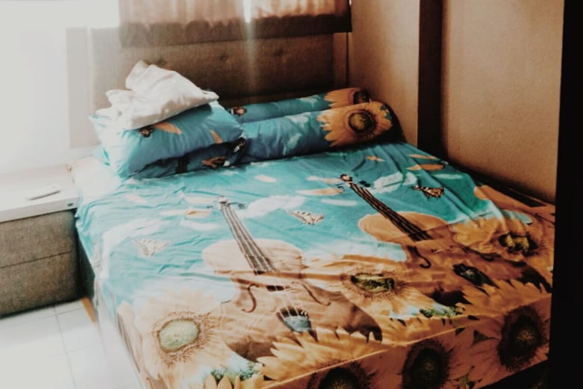 A bedroom with a bed, pillows, a window with curtains, and an air conditioning unit.