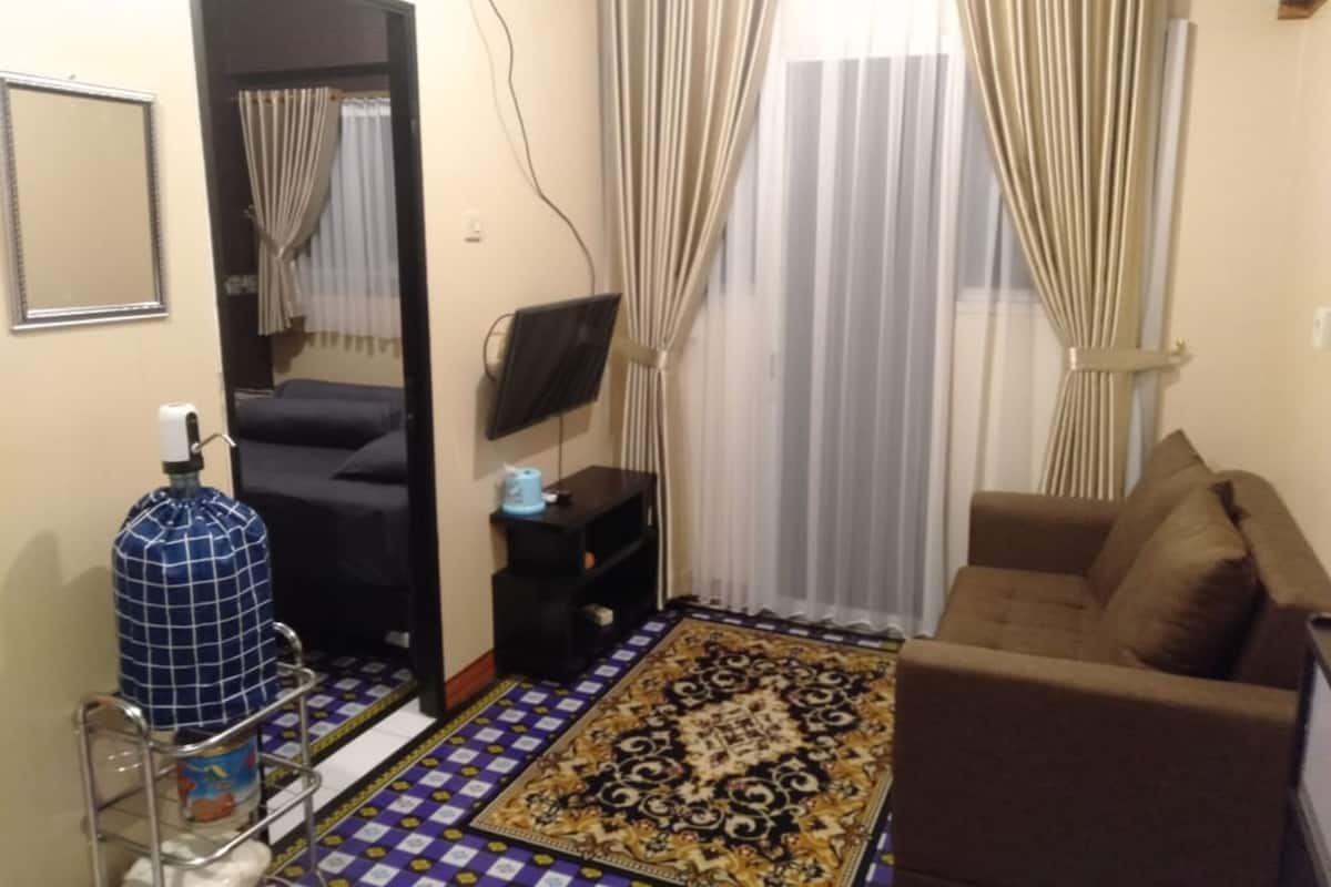 A living room with a sofa, a television on a stand, a patterned rug, and a mirror on the wall.
