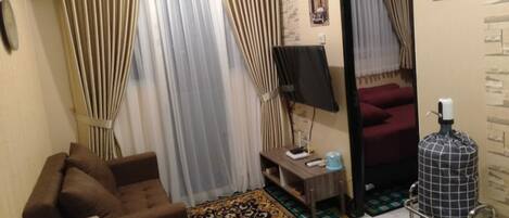 Un espacio habitable pequeño con un sofá, una mesita, una lámpara, un radiador, un espejo y una alfombra estampada.