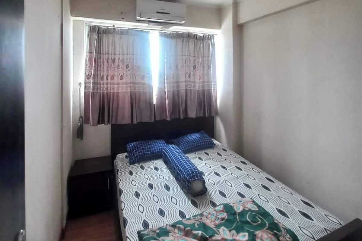 A small, single-bed room with a window, a ceiling fan, and an air conditioning unit.
