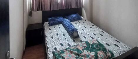 Een kleine kamer met een enkel bed, raam, plafondventilator en airconditioning.