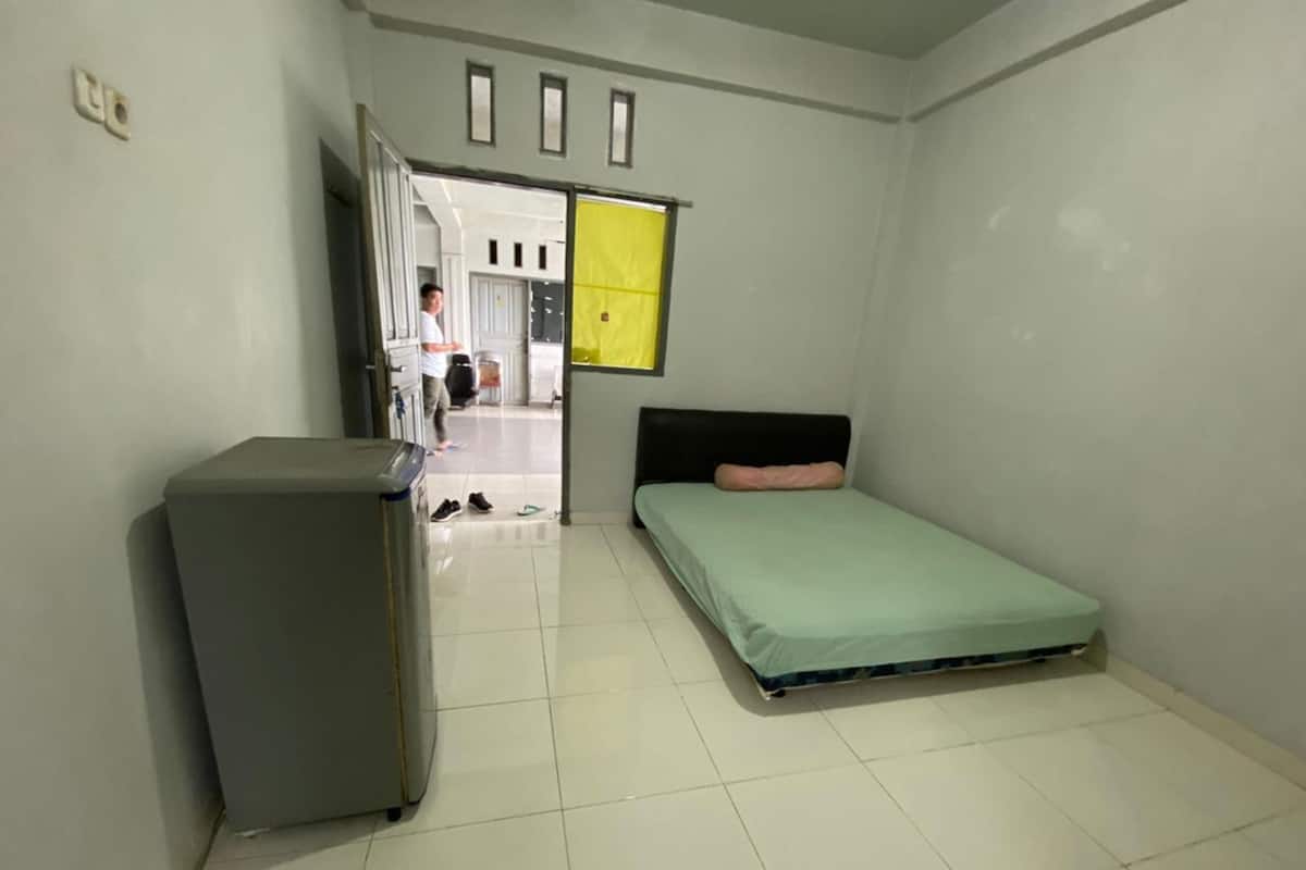 A small, clean room with a bed, a desk, and a door leading to a hallway.