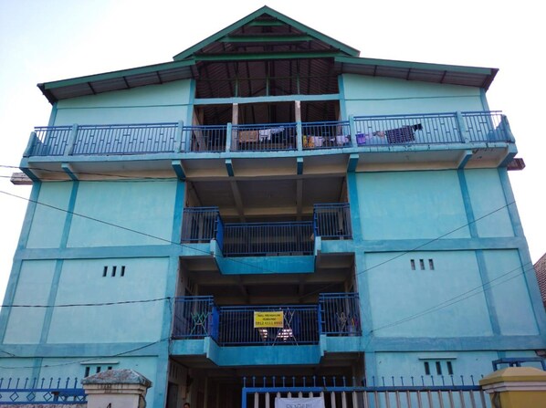A multi-story building with balconies, a signboard, and a blue fence.