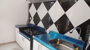 A compact kitchen with a gas stove, a sink, and a backsplash with a black and white diamond pattern. - Cassa Mia Villa 1 (Sleman)