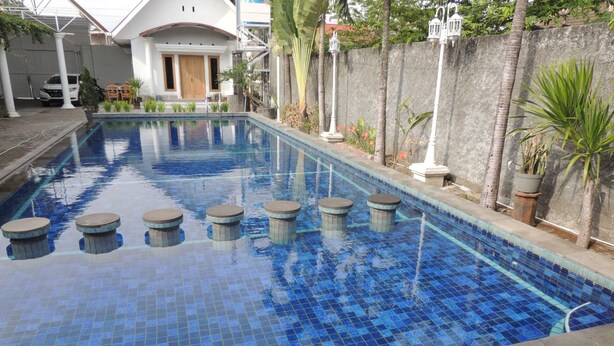 A swimming pool with blue tiles, surrounded by a concrete deck and potted plants. - Cassa Mia Villa 1 (Sleman)