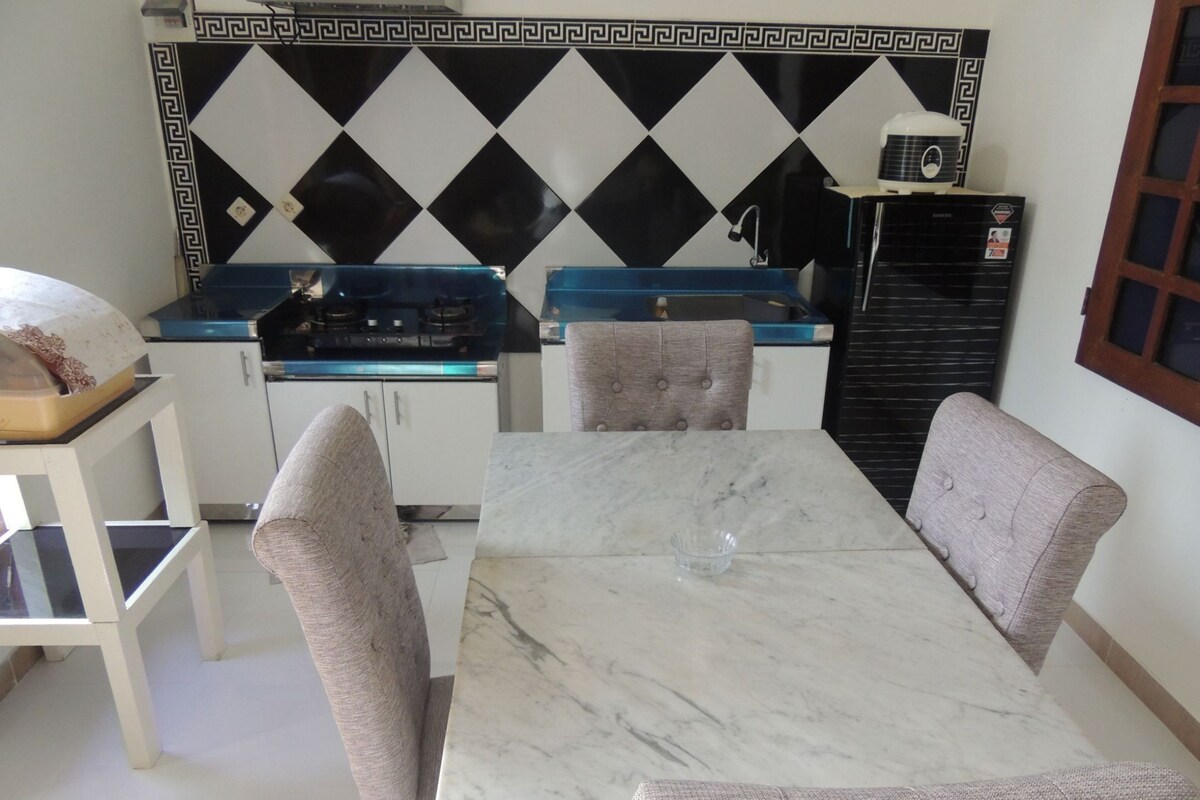 A kitchen with a marble table, two upholstered chairs, a blue countertop, and a black refrigerator.