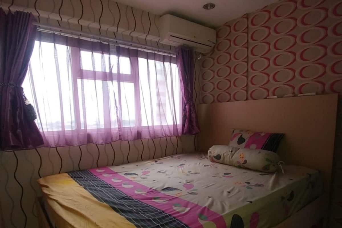 A bedroom with a bed, curtains, an air conditioning unit, and patterned wallpaper.