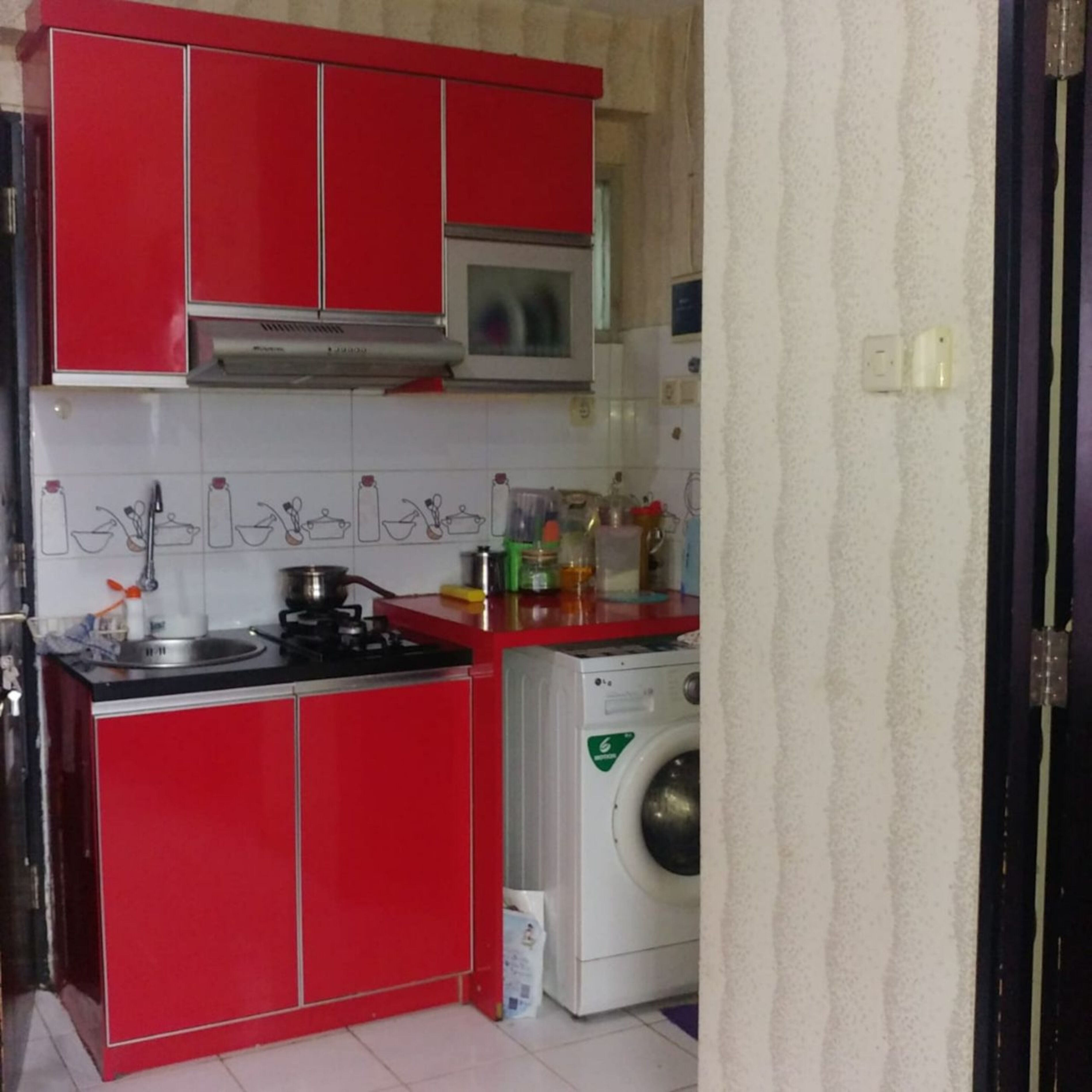 A compact kitchen with red cabinets, a microwave, a washing machine, and a sink.