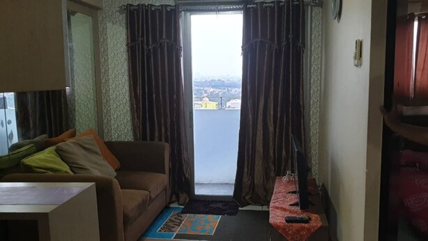 En stue med en sofa, et lille bord og udsigt over en by gennem et vindue med gardiner.