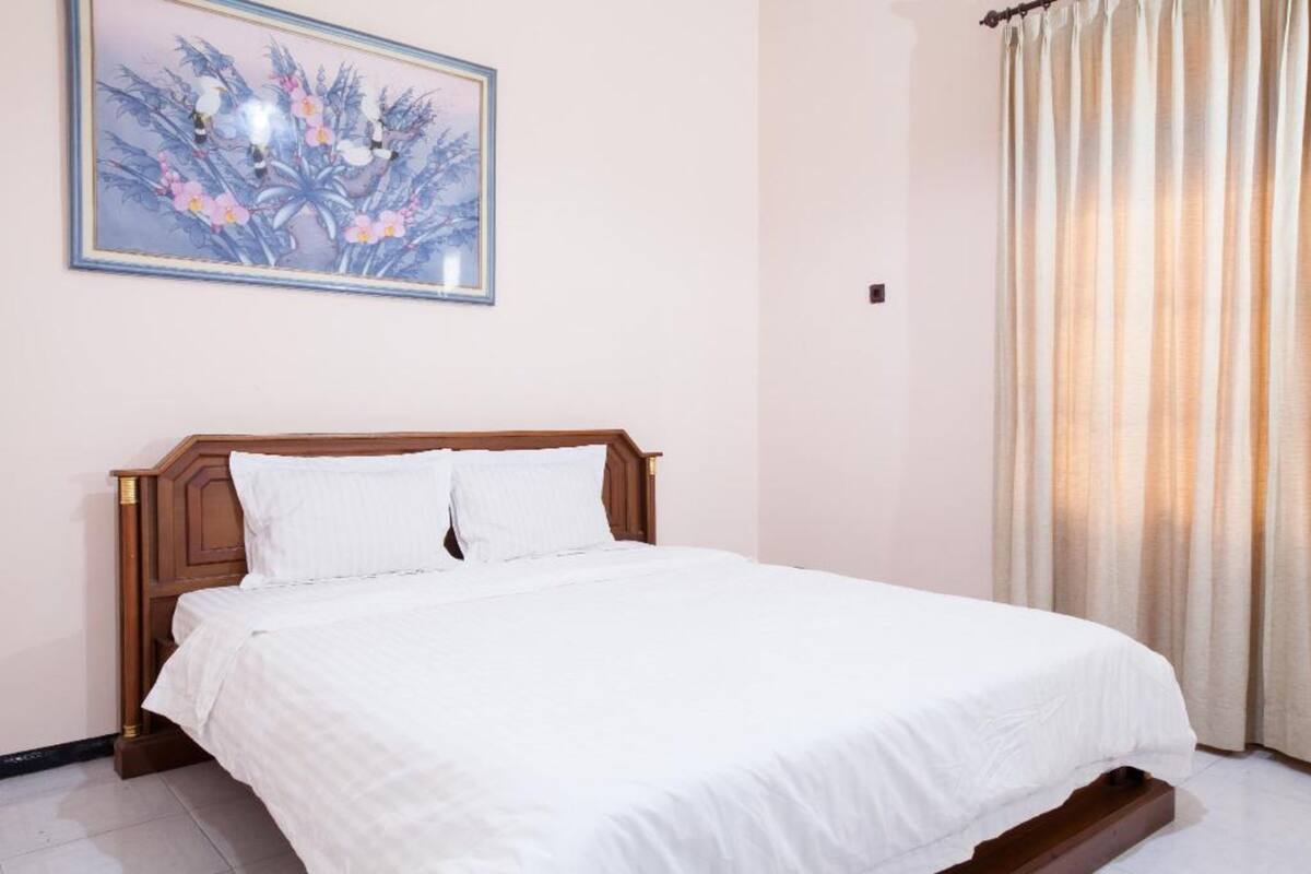 A neatly made bed with white linens in a room with a wooden headboard.