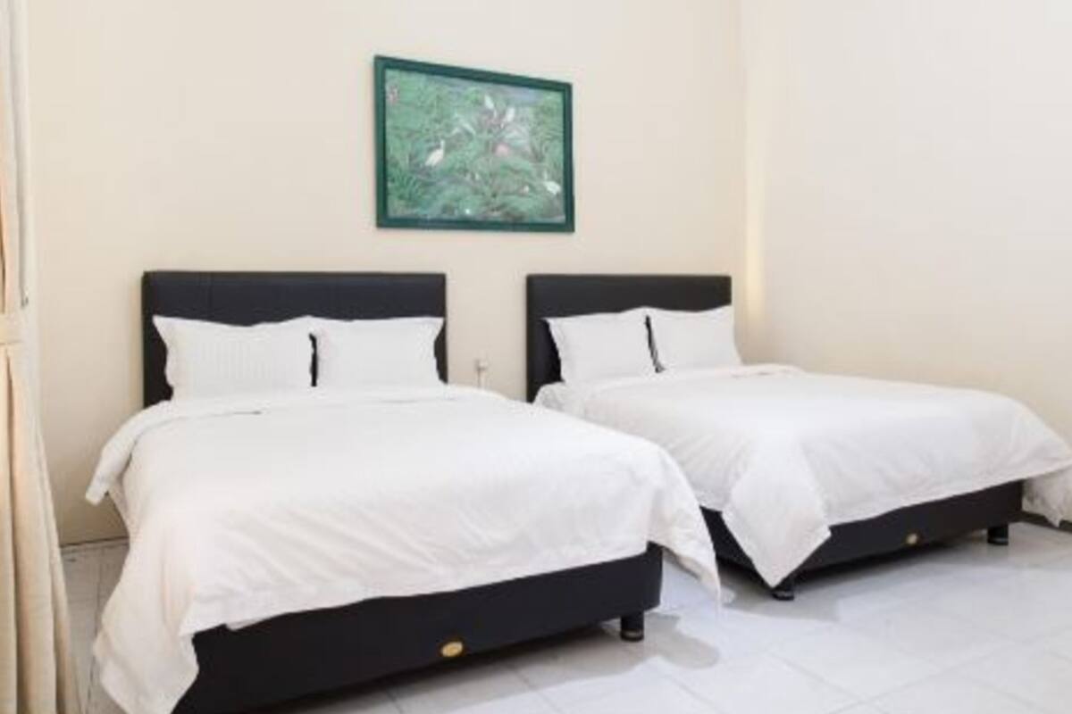 Two single beds with white bedding in a room with a green framed picture on the wall.