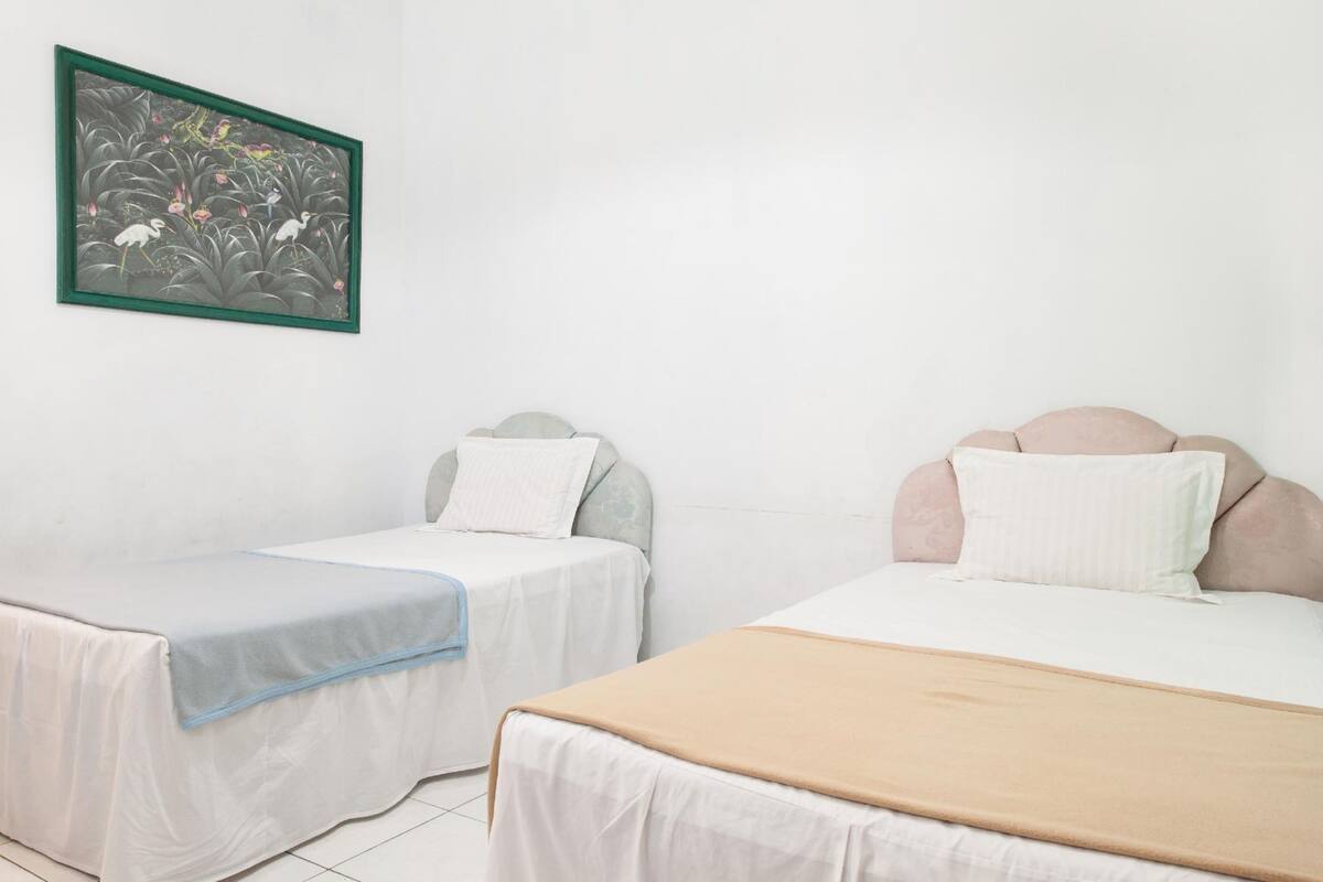 Two single beds with different headboards, a framed artwork on the wall, and a white tiled floor.
