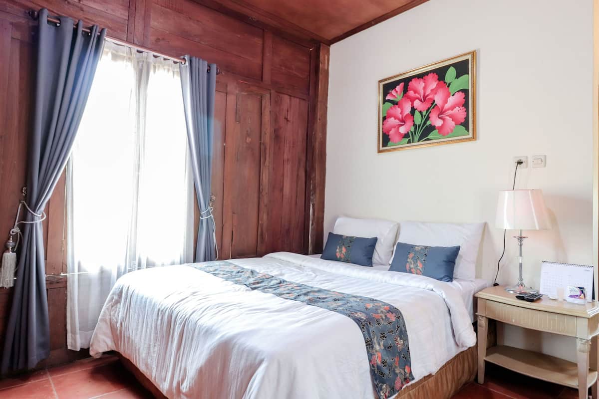 Ein Schlafzimmer mit einem hölzernen Kopfende, einem Bett mit weißer und blauer Bettwäsche, einem Nachttisch mit einer Lampe und einem floralen Gemälde an der Wand.