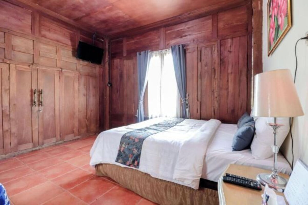 A wooden room with a bed, a TV mounted on the wall, and a window with curtains.