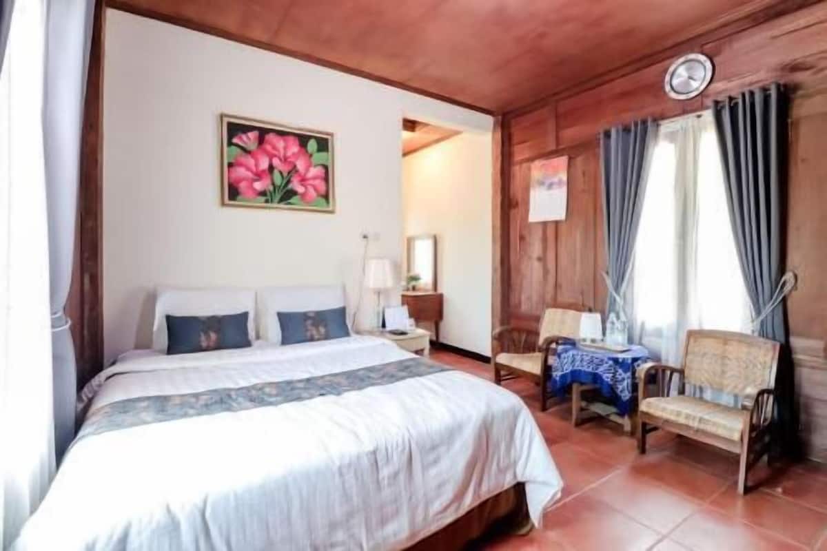 Ein Schlafzimmer mit Bett, Stuhl, Tisch, einem Gemälde und einer Uhr.