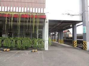 A parking garage entrance with a covered walkway, concrete pillars, and a green directional sign. - Studio Room at V Apartment (Depok)