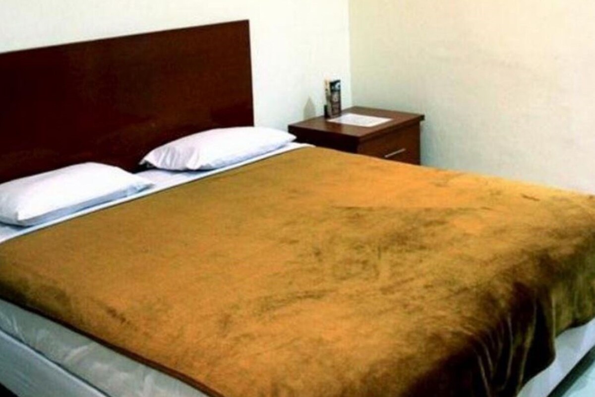Una cama individual con una manta marrón, un cabecero de madera y una mesita de noche con una lámpara.