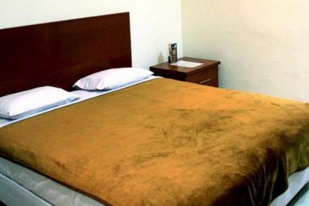 Een enkel bed met een houten hoofdbord, een wit kussen en een bruine deken.