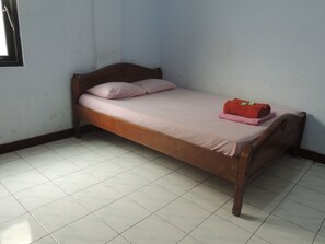 A single bed with a wooden frame and a pink mattress, a red towel, and a pink pillow in a room with white tiled flooring and light blue walls. - Hotel Sejahtera (Kebumen)