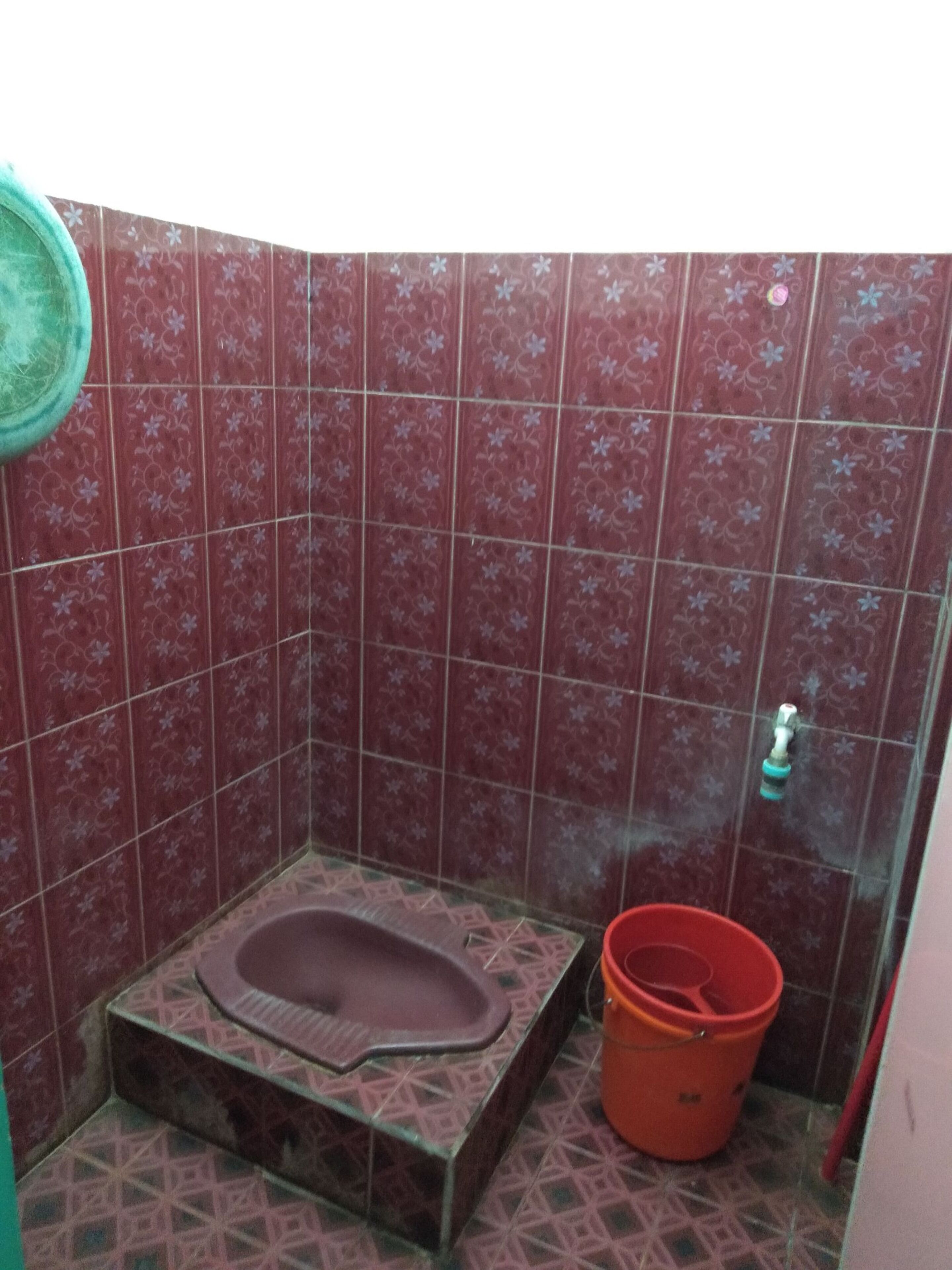 A small bathroom with a toilet, a red bucket, and patterned tiles.