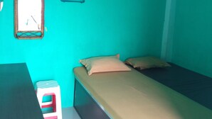 A small, single-bed room with teal walls, a small window, a hanging clothes hanger, and a desk with a chair. - KOST 748 AT (Medan)