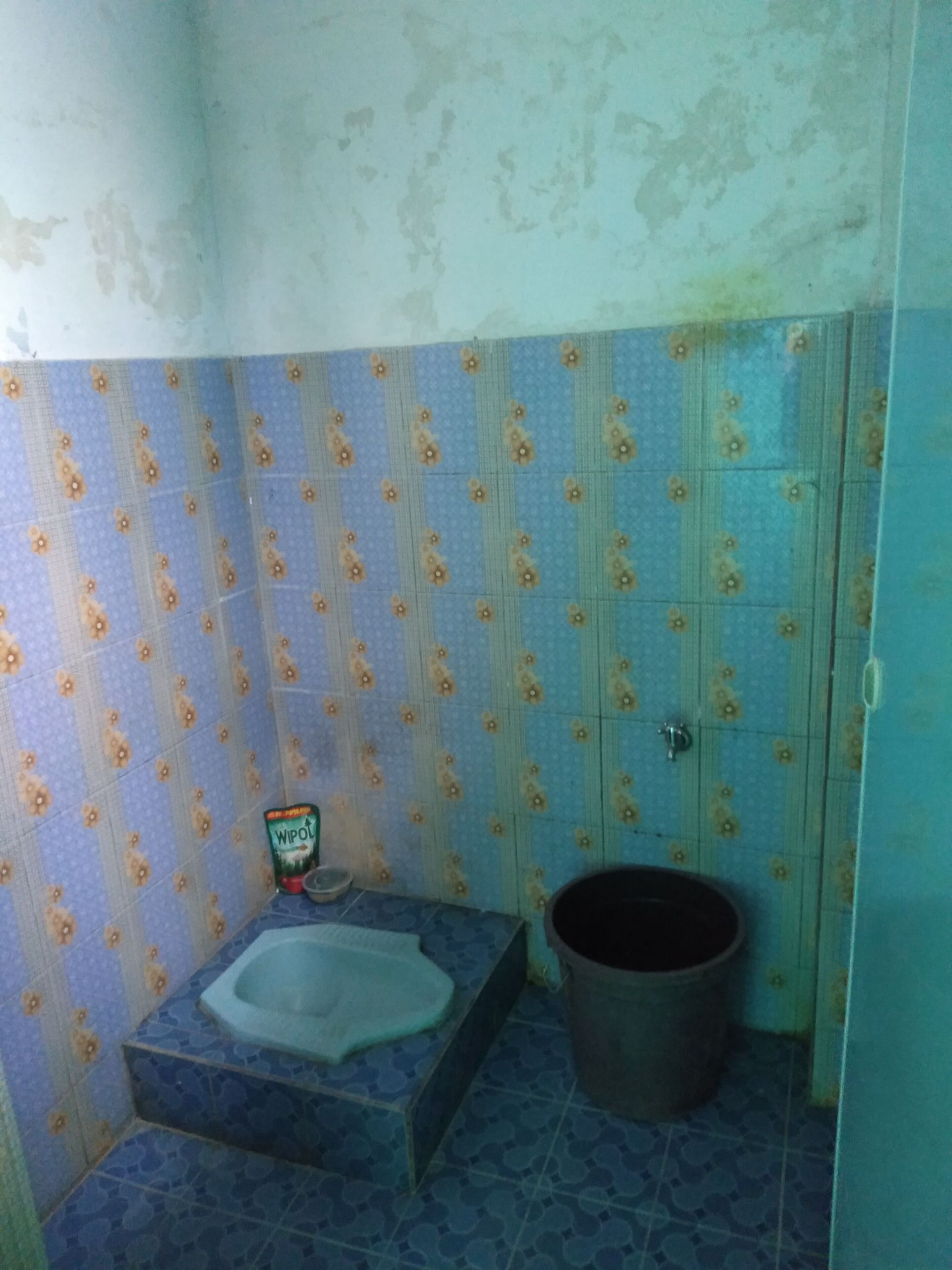 A bathroom with a toilet, a bucket, and patterned tiles.