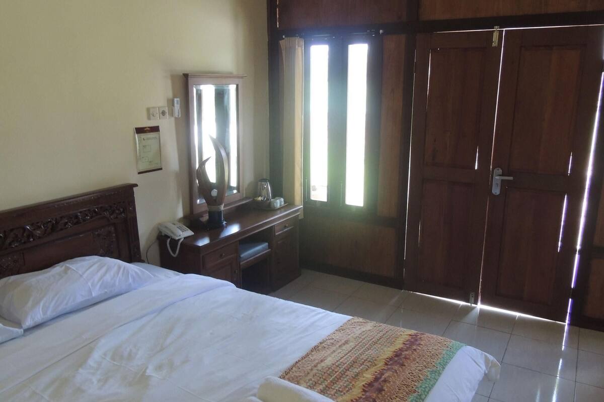 A hotel room with a bed, a dresser, a mirror, a telephone, and a wardrobe.