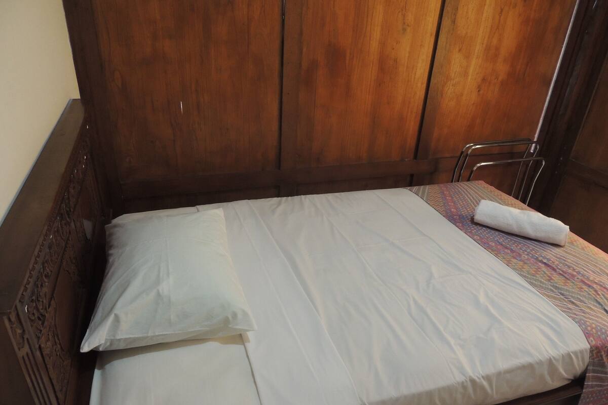 A single bed with white bedding, a wooden headboard, and a patterned tablecloth on the nightstand.