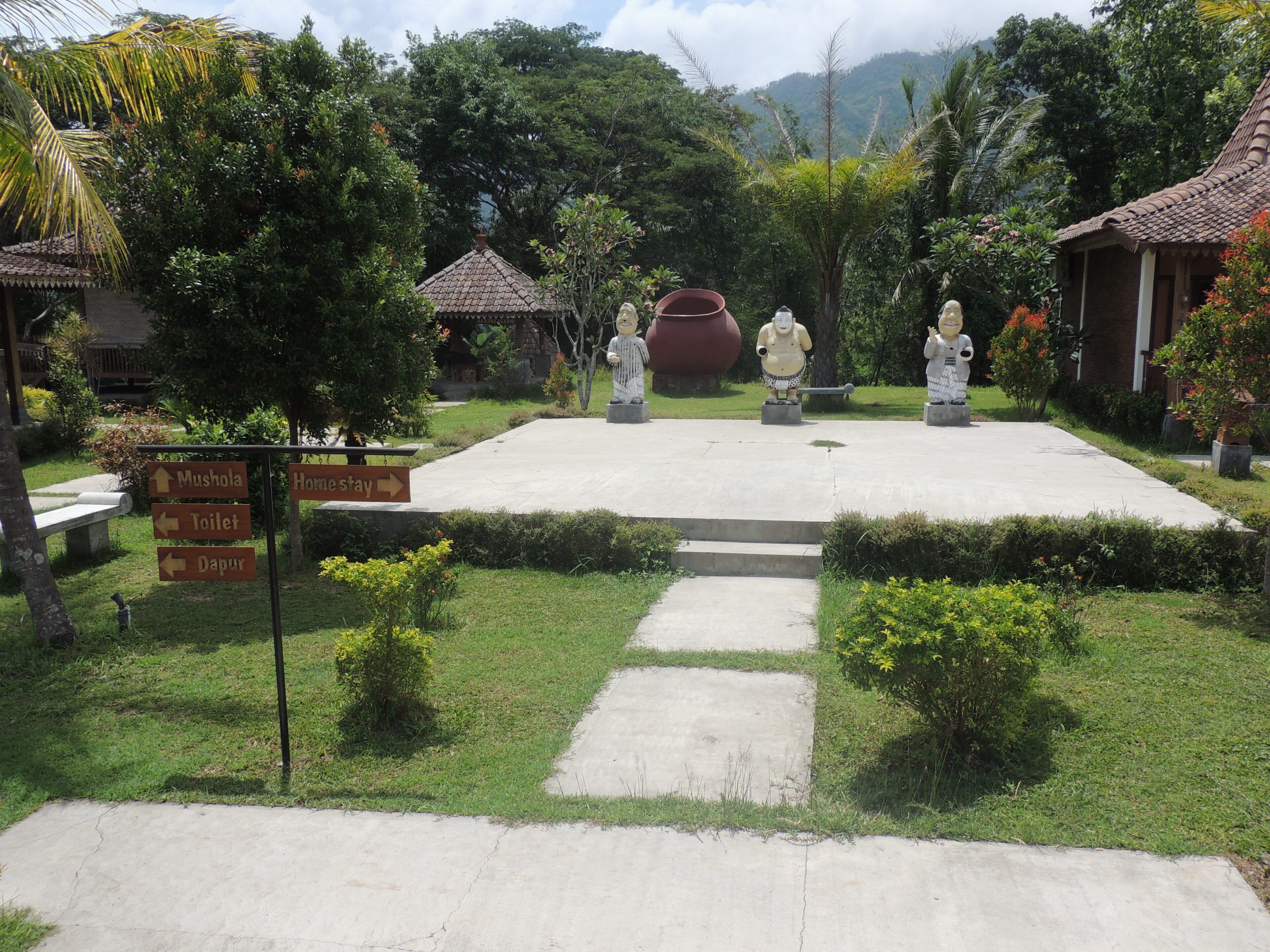 A courtyard with statues, a signpost with directions, and a building with a tiled roof.