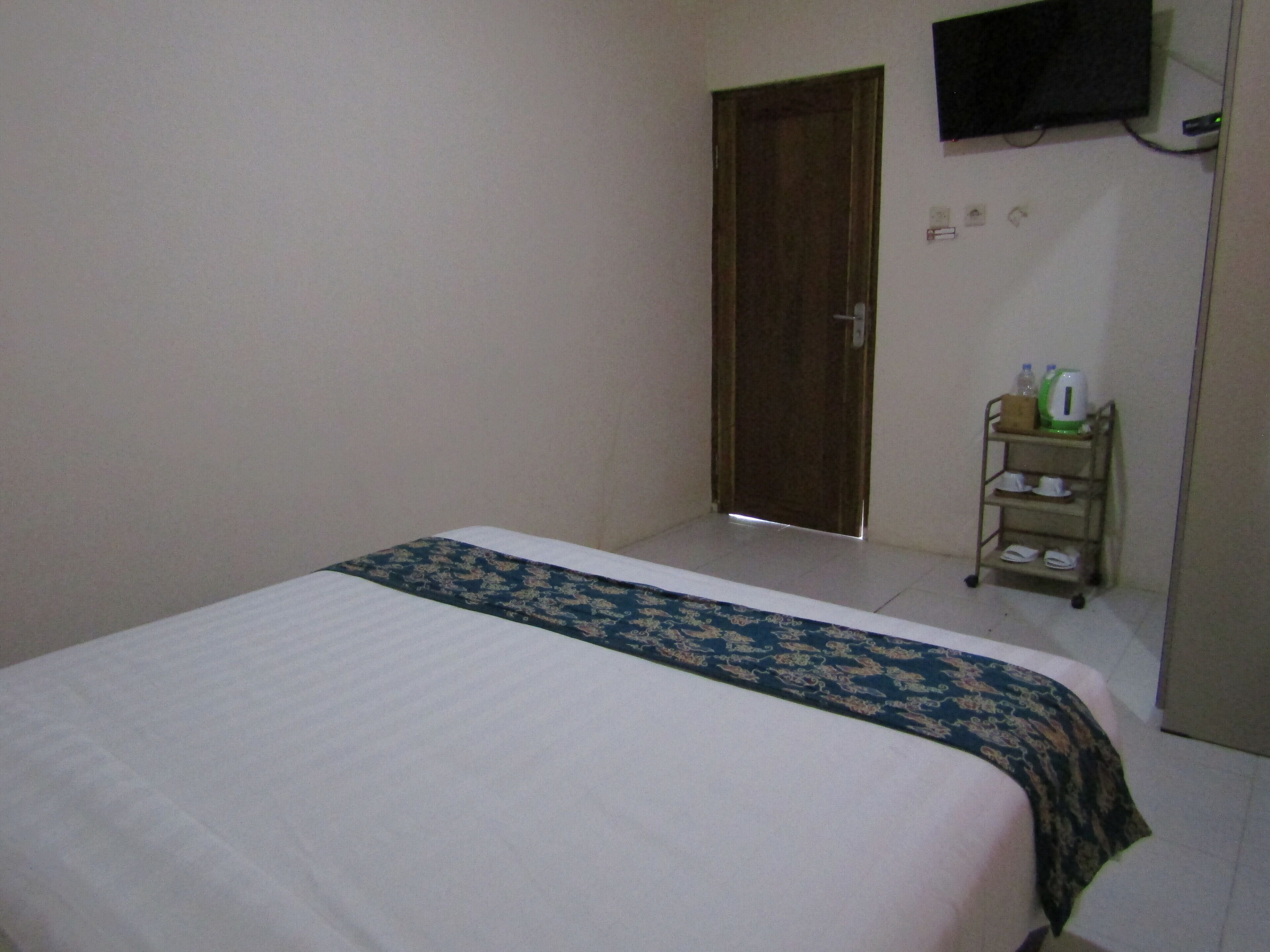 Une chambre d’hôtel avec un lit, un téléviseur fixé au mur et une petite étagère contenant des articles de toilette.