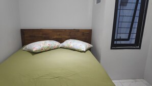 A single bed with a wooden headboard, a green bedspread, and two floral-patterned pillows. - Avicenna 2 Guesthouse (Demangsari)