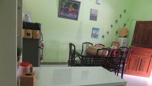 A dining area with a glass table, wooden chairs, and a woven table runner. - Avicenna 2 Guesthouse (Demangsari)